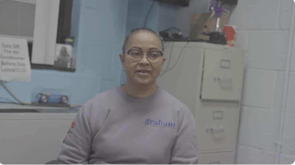 Still from the series: a woman in a lavender sweatshirt speaking to camera in an office, filing cabinets behind her.