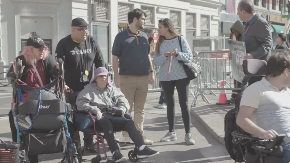 Still from the documentary: wheelchair users and advocates gathered on a New York City street at a transit accessibility demonstration.